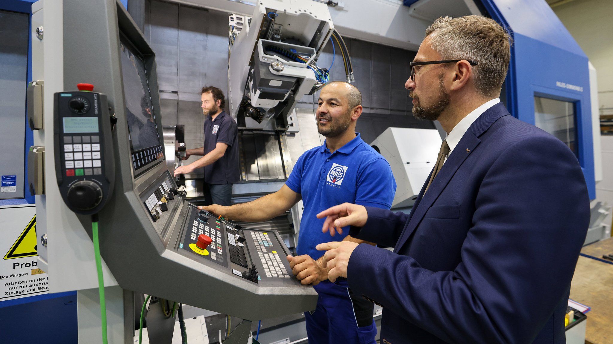 Ein Mann erklärt einem zweiten Mann die Bedienung einer großen Dreh-Fräs-Maschine