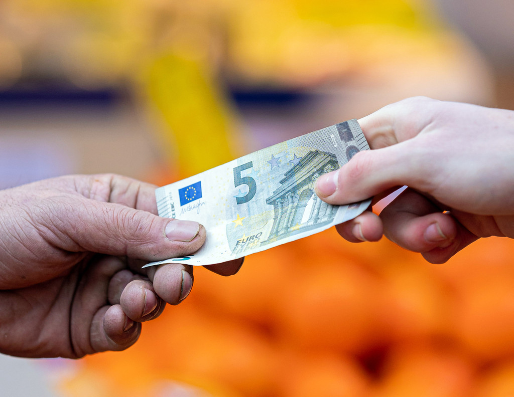 Ein Kunde bezahlt seinen Einkauf an einem Stand auf einem Wochenmarkt mit einem Fünf-Euro-Schein (gestellte Szene).