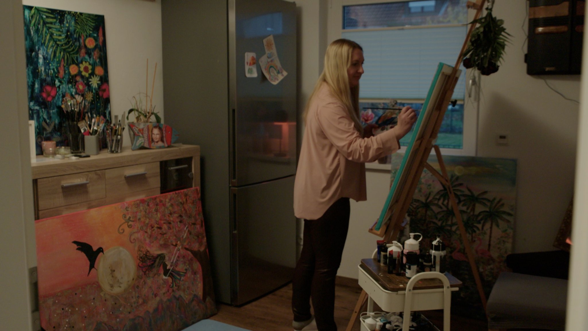 Eine Frau steht an einer Staffelei und malt. 
