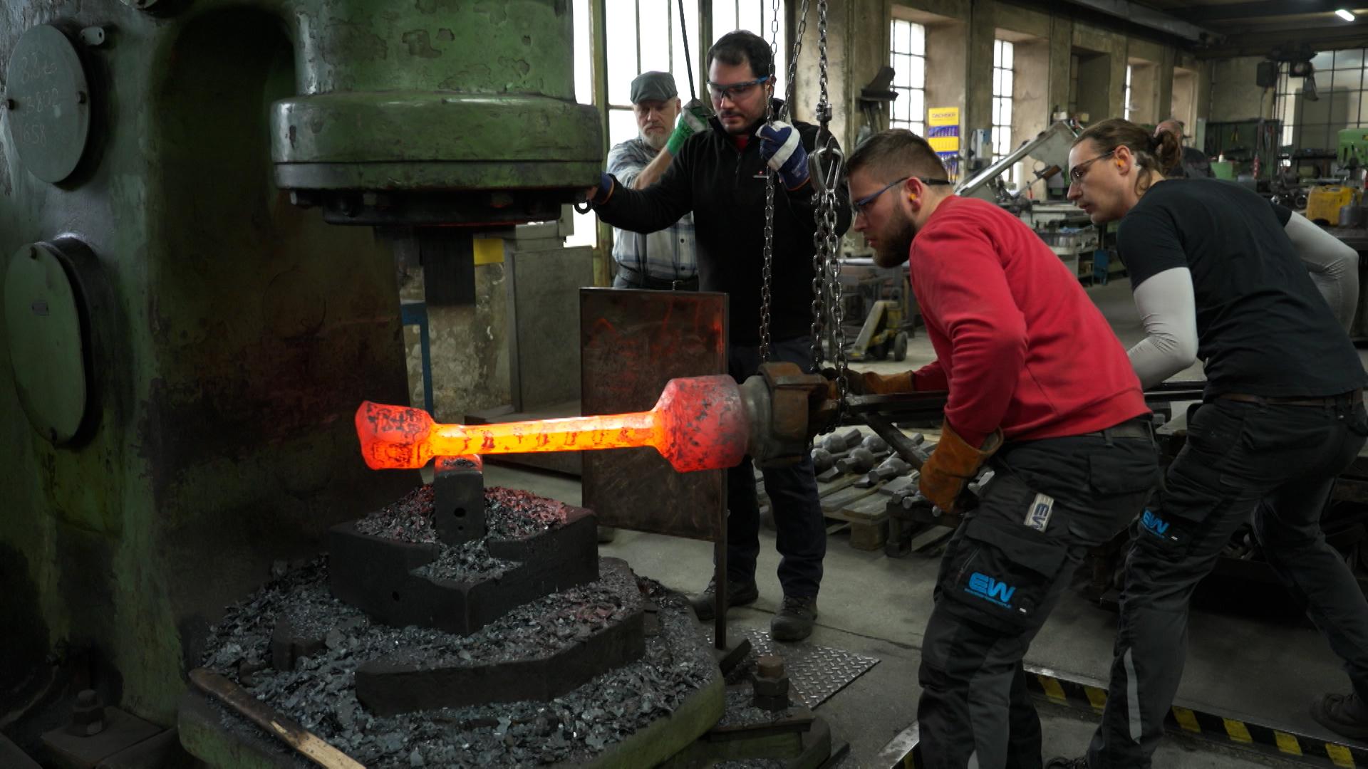 Drei Männer schmieden Glockenklöppel