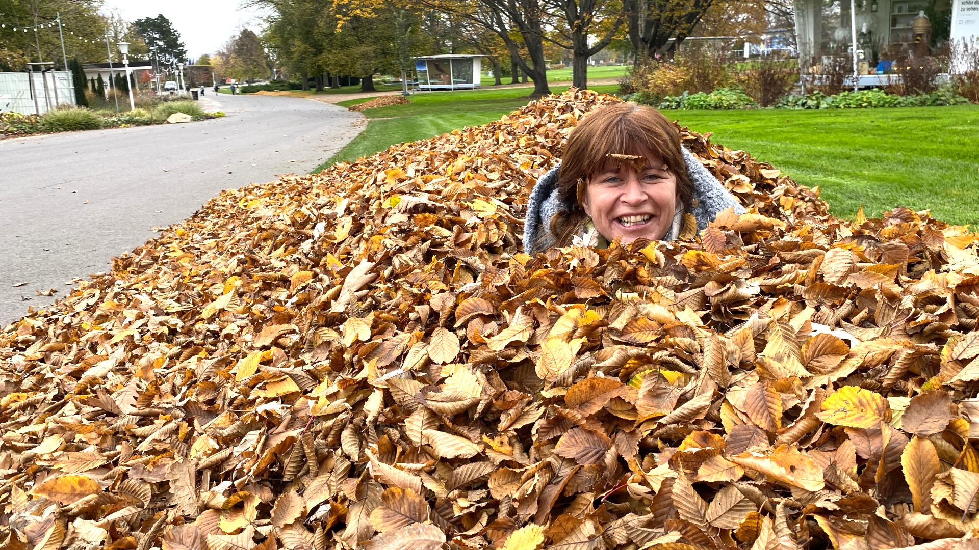 Querbeet-Expertin Sabrina Nitsche schaut nur noch mit dem Kopf aus einem großen Laubhaufen hervor.