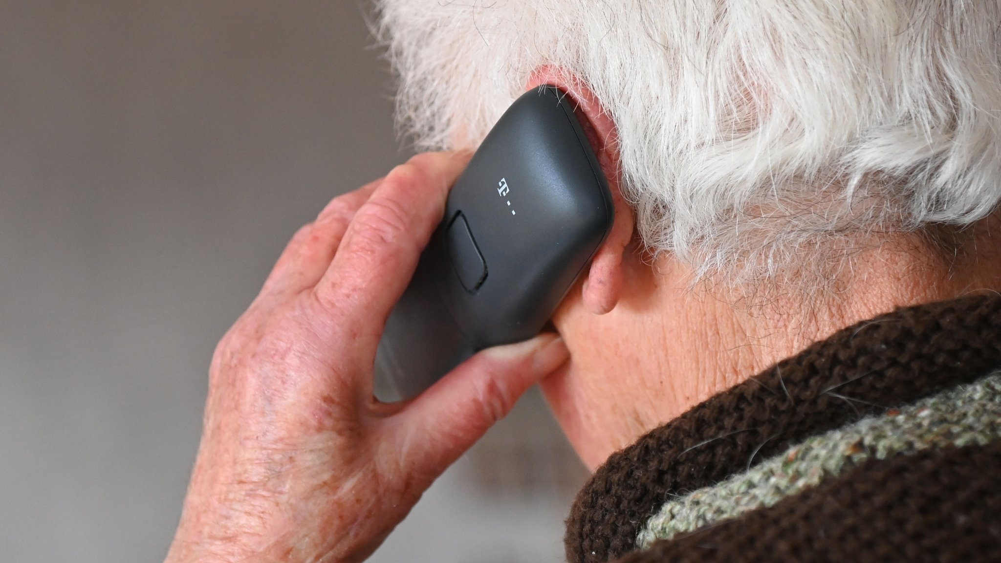 Ein älterer Mann hält sich ein Telefon ans Ohr.