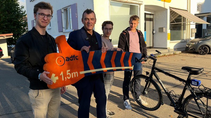 Studierende der Hochschule Kempten und Professor Thomas Zeh (zweiter v.l.) halten eine 1,5 Meter lange Messlatte an einen Fahrradlenker. | Bild: BR/Reichart Studierende der Hochschule Kempten und Professor Thomas Zeh (zweiter v.l.) halten eine 1,5 Meter lange Messlatte an einen Fahrradlenker.