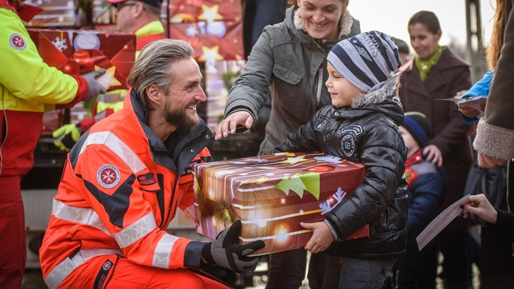 Ein Mitarbeiter der Johanniter übergibt ein Weihnachtpäckchen an ein Kind