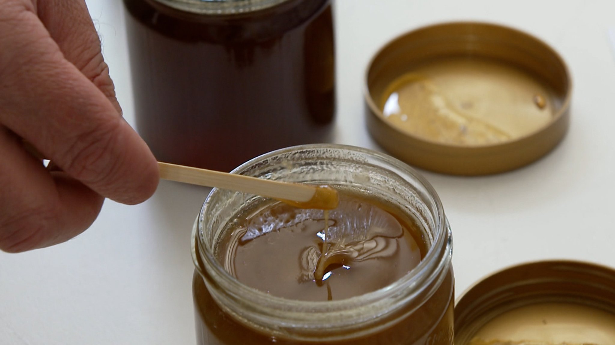 Hand entnimmt mit Holzstäbchen Honig aus Glas