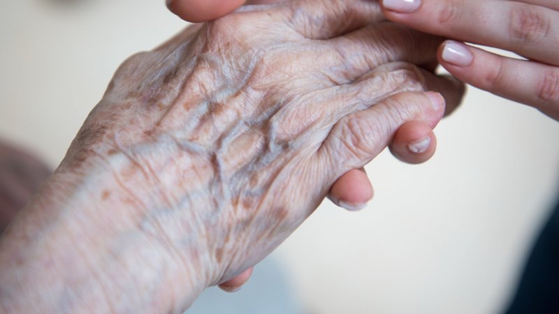 Eine Pflegerin hält die Hand einer Bewohnerin in einem Seniorenzentrum. | Bild: dpa-Bildfunk/Christophe Gateau Eine Pflegerin hält die Hand einer Bewohnerin in einem Seniorenzentrum.