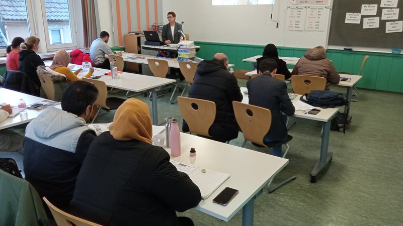 Deutschunterricht für Geflüchtete an der VHS Rhön und Grabfeld: Die erwachsenen Teilnehmenden sitzen in einem Kursraum und verfolgen den Unterricht der Lehrerin.