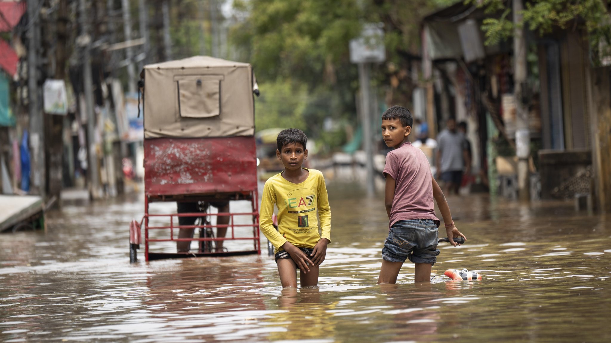 ARCHIV (28.04.2025): Kinder waten durch eine überschwemmte Straße nach schweren Regenfällen in Guwahati, Indien, am 28. April 2025, Asien