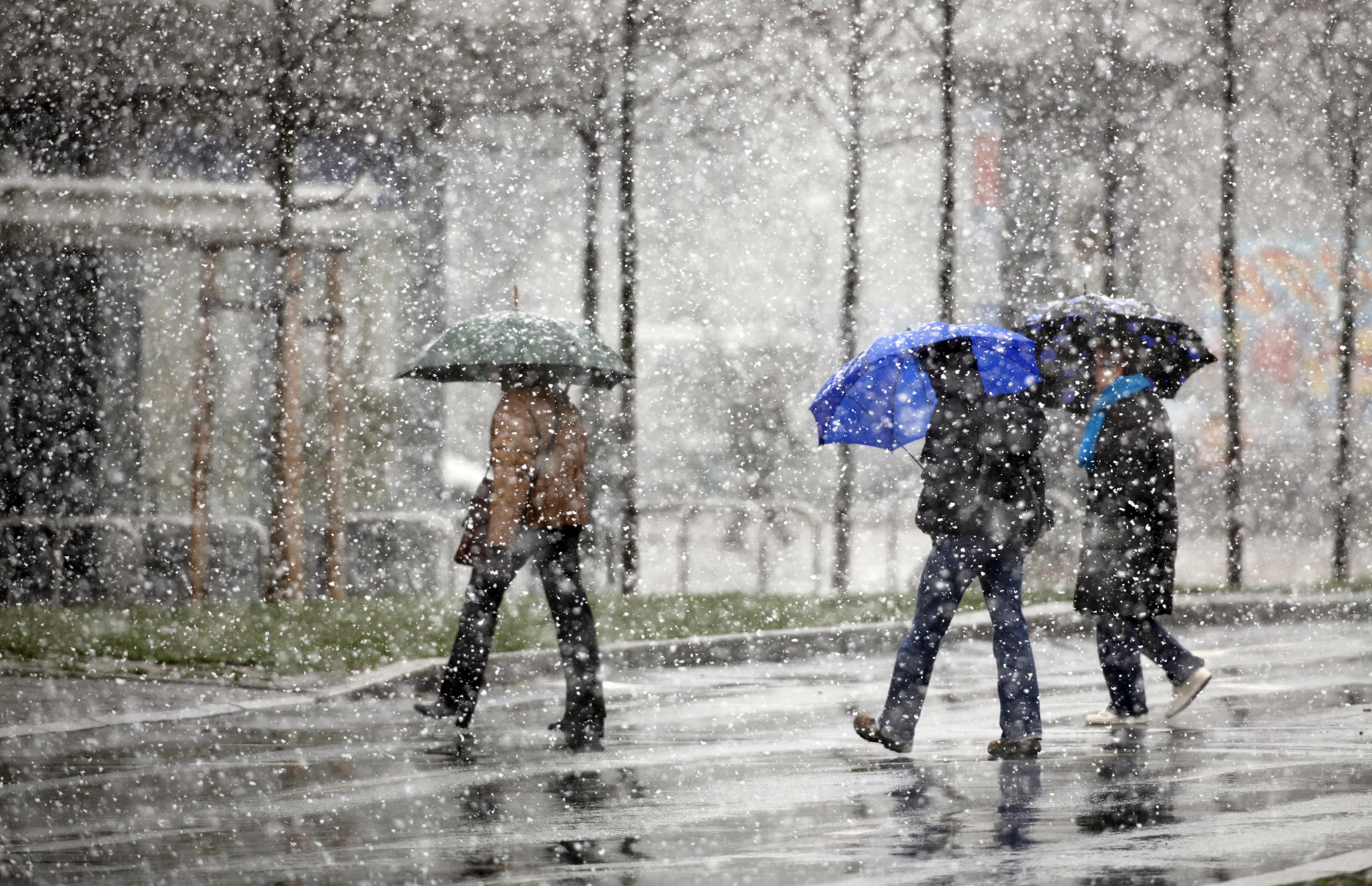 Menschen mit Schirmen gehen bei Schneeregen über eine Straße.