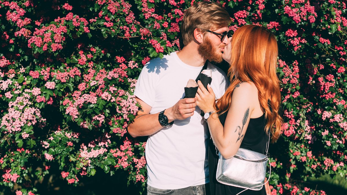 Frühlingsgefühle: Knutschendes junges Paar im Park mit Eiscreme in der Hand.