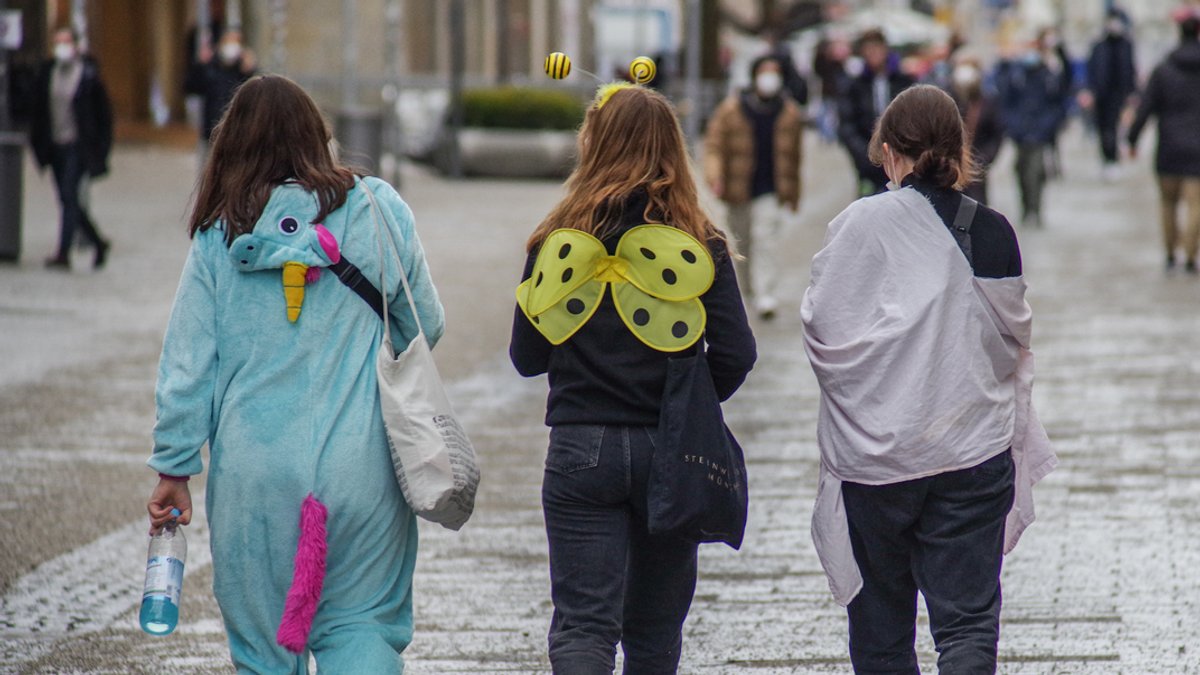 Drei junge Frauen in Faschingsverkleidung von hinten: Einhorn-Anzug, Bienenflügel und Gespensterumhang.