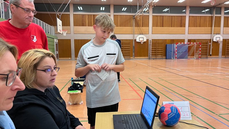 Handballschiedsrichter schaut in Turnhalle auf einen Laptop mit Spieldaten