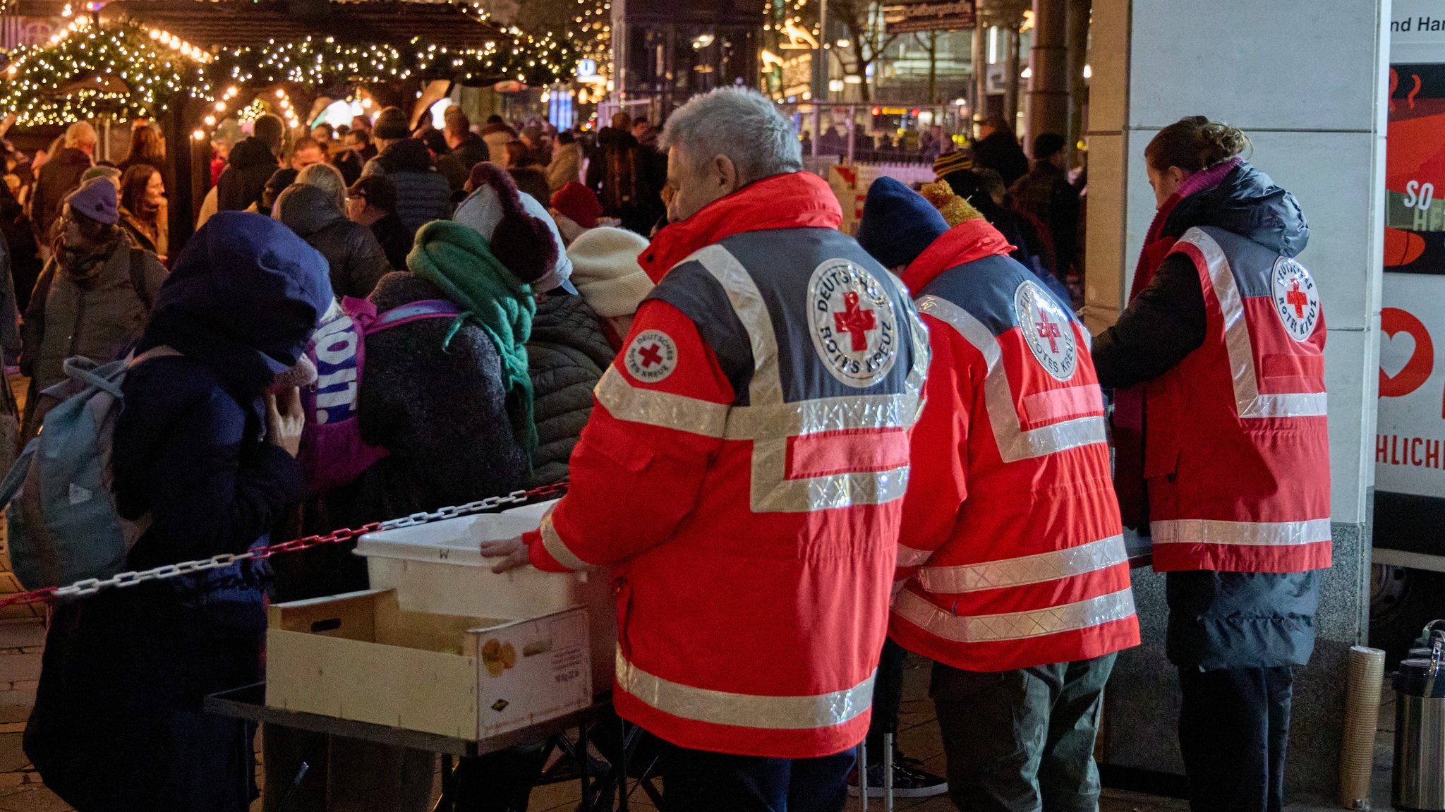  Ehrenamtliche Mitglieder des Deutschen Roten Kreuzes (DRK) verteilen Lebensmittel an obdachlose Menschen.