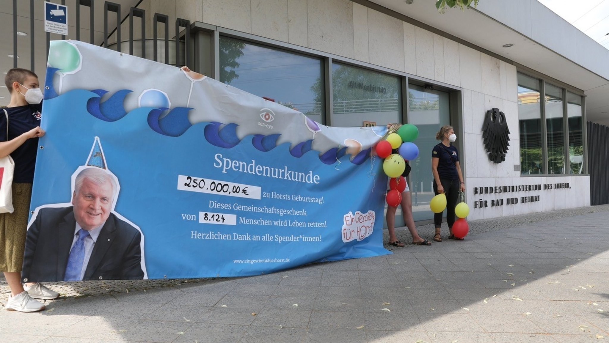 Mitglieder von Sea-Eye, die ein großes Banner mit der Spendenurkunde überreichen wollen.