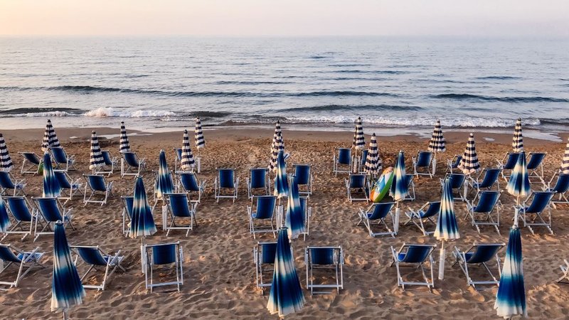 An einem Strand in Italien stehen aufgeklappte Liegen und zugeklappte Sonnenschirme, alle in blau-weiß, direkt am Meer. Der Sonnenschirm bleibt zu, die Liege wird nicht aufgeklappt: Italiens Strandbäder sind im Streik – allerdings erst einmal nur für eine halbe Stunde. | Bild: BR/Sylvia Bentele An einem Strand in Italien stehen aufgeklappte Liegen und zugeklappte Sonnenschirme, alle in blau-weiß, direkt am Meer. Der Sonnenschirm bleibt zu, die Liege wird nicht aufgeklappt: Italiens Strandbäder sind im Streik – allerdings erst einmal nur für eine halbe Stunde.