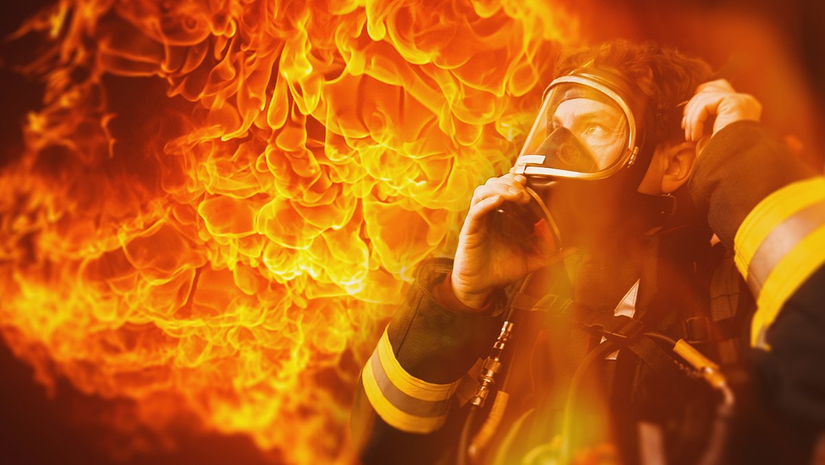 Feuerwehrmann mit Atemschutzmaske vor Feuerwand