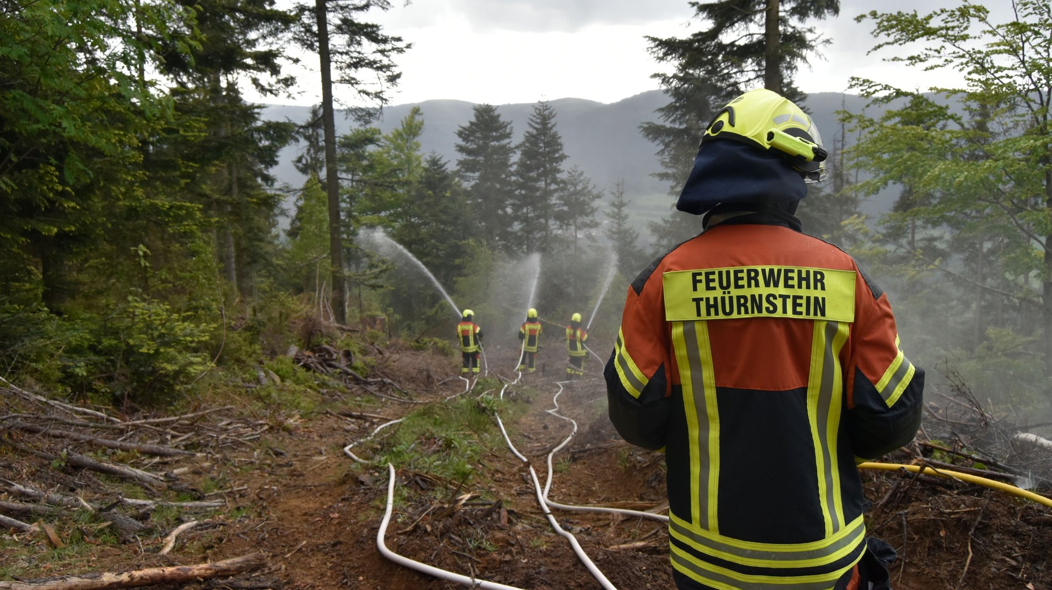 Einsatzkräfte der Feuerwehr verspritzen aus Feuerwehrschläuchen Wasser im unwegsamen, bewaldeten Gelände | Bild: Kreisbrandinspektion Cham Einsatzkräfte der Feuerwehr verspritzen aus Feuerwehrschläuchen Wasser im unwegsamen, bewaldeten Gelände