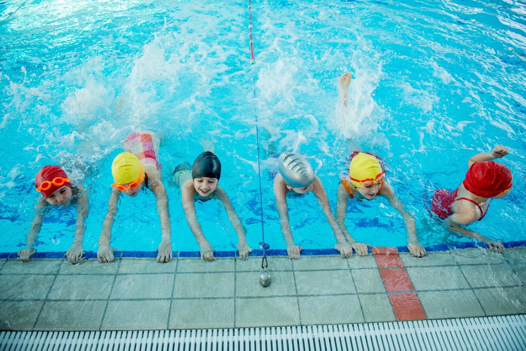 Eine Gruppe von Mädchen übt am Beckenrand eines Schwimmbeckens Schwimmen.