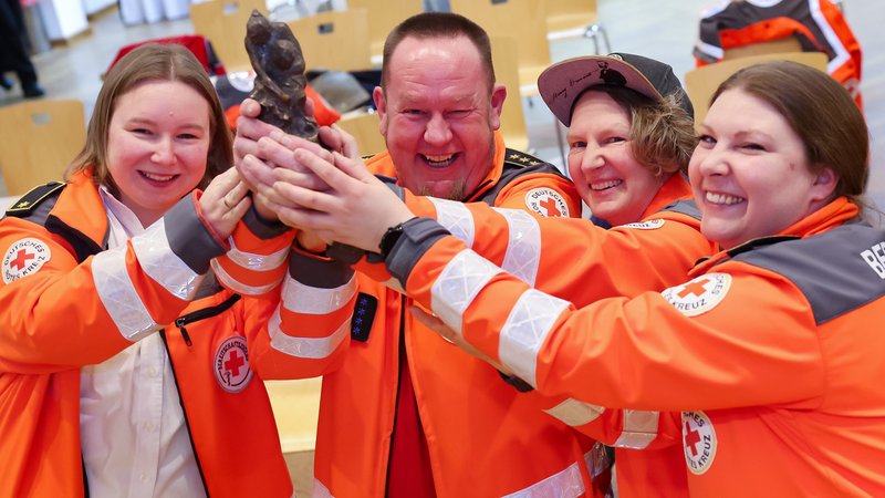 BRK-Mitarbeiter in orangefarbener Arbeitskleidung halten lachend ihre Trophäe in die Höhe.