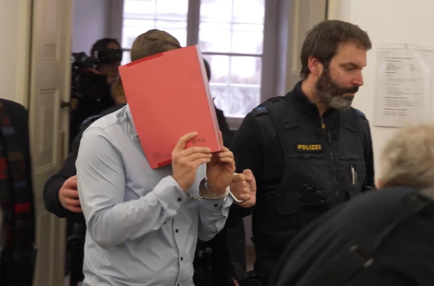 Der Angeklagte verbirgt beim Betreten des Gerichtssaals sein Gesicht hinter einem roten Ordner. 