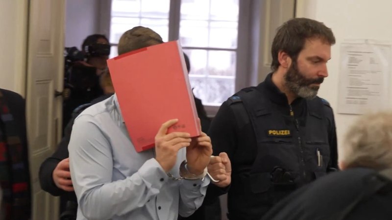Der Angeklagte verbirgt beim Betreten des Gerichtssaals sein Gesicht hinter einem roten Ordner. 