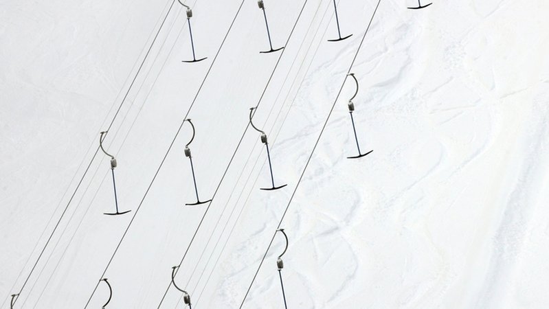Bügel hängen an einem Schlepplift, darunter eine verschneite Piste (Symbolbild).