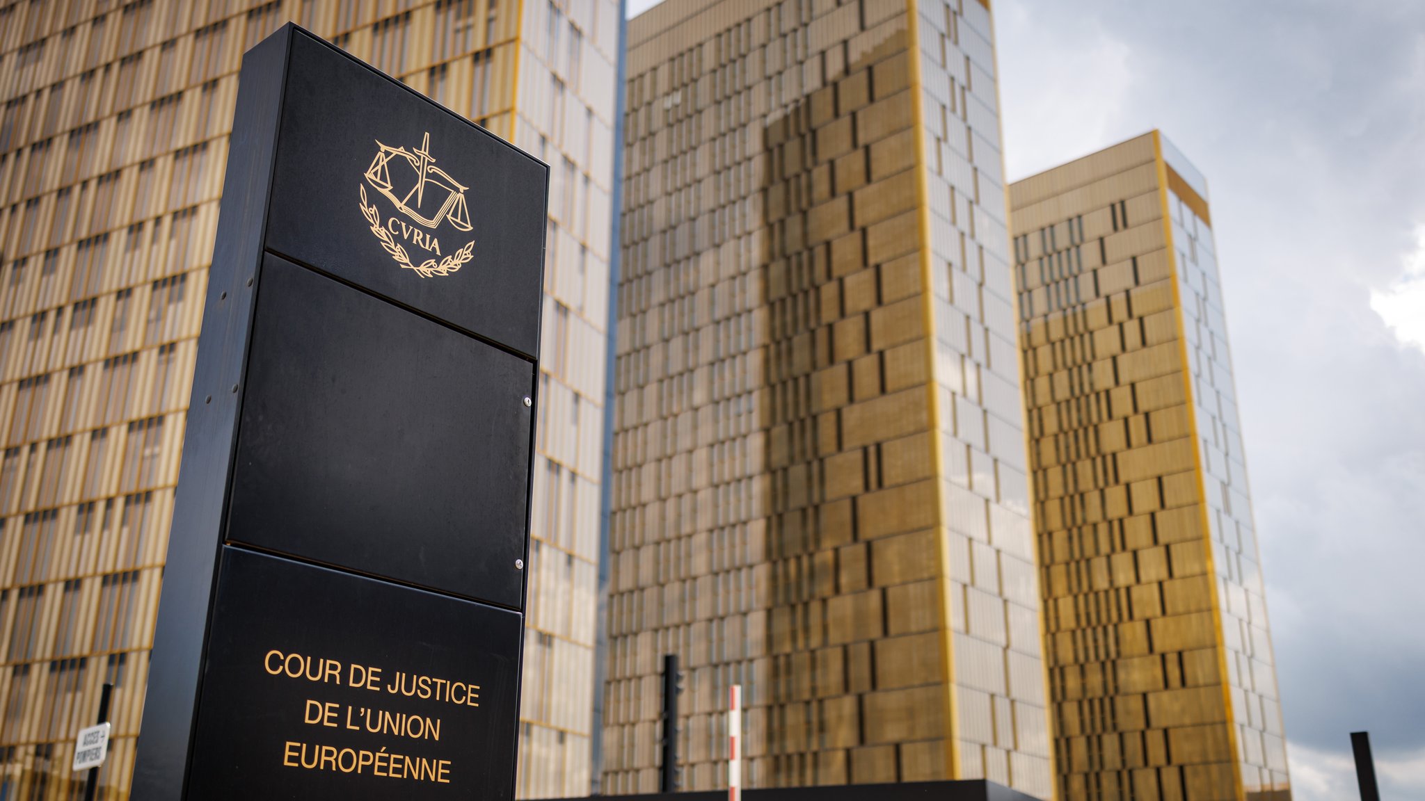 Eine Stele mit der Aufschrift "Cour de Justice de l'union Européene" steht an einem Eingangsbereich am Europäischen Gerichtshof (EuGH) im Europaviertel.