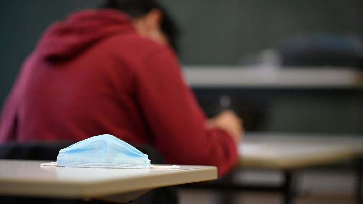 Ein Schüler sitzt in einem Klassenzimmer, ein Mundschutz liegt auf dem Tisch.