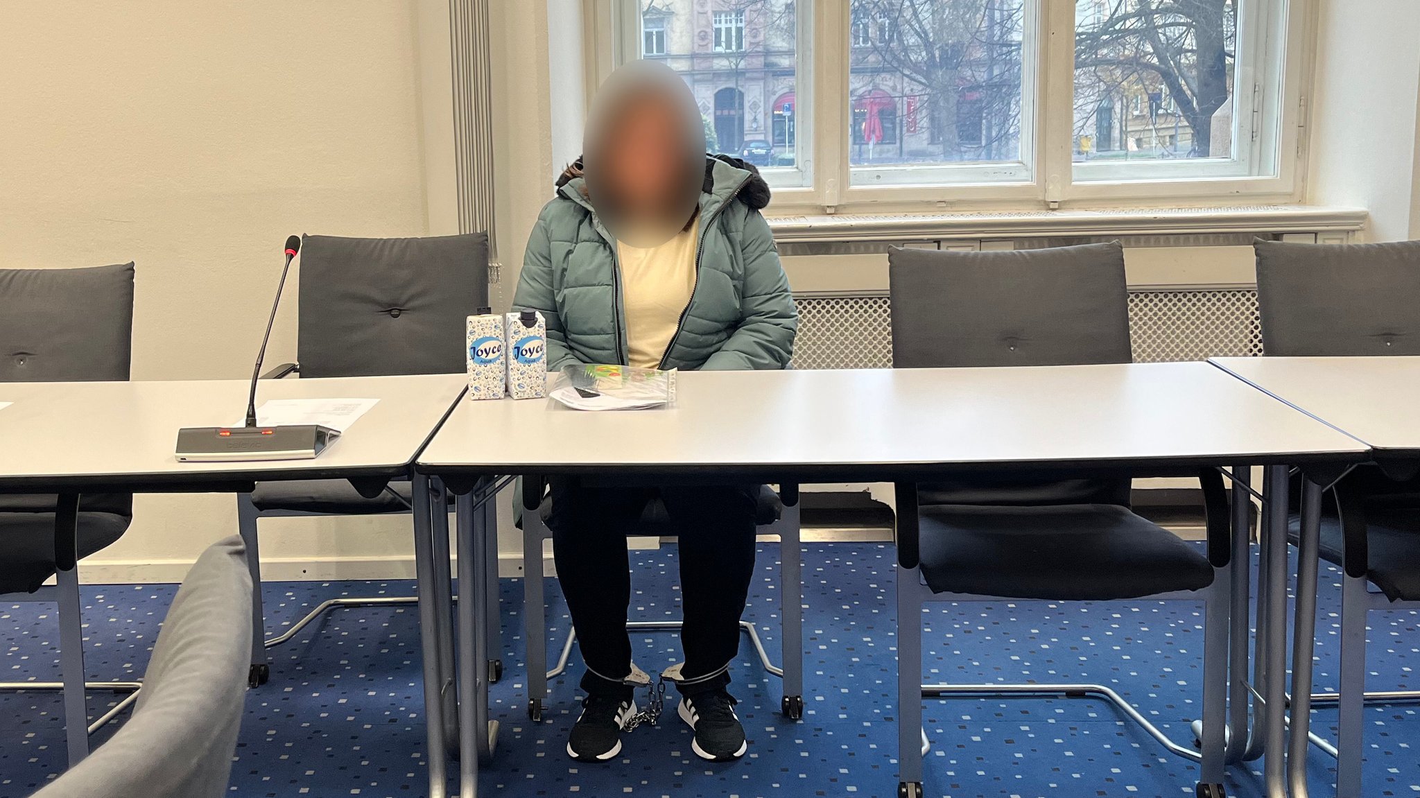 Die Angeklagte sitzt mit Fußfesseln an einem Tisch im Verhandlungssaal. 