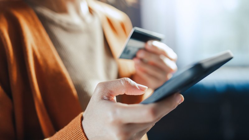 Ein Frau hält ein Smartphone und ihre Kreditkarte in Händen. | Bild: stock.adobe.com/oatawa Ein Frau hält ein Smartphone und ihre Kreditkarte in Händen.