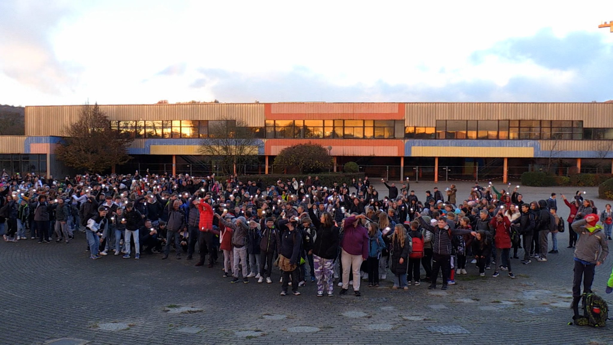 Schülerinnen und Schüler halten ihre Handys vor der Schule in die Höhe.