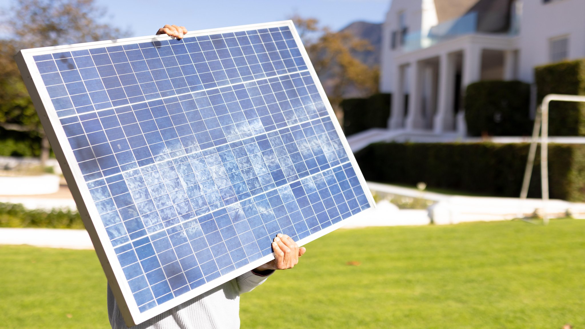 Eine Person hält ein kleines Solarpaneel in die Sonne, im Hintergrund ist Frühling.