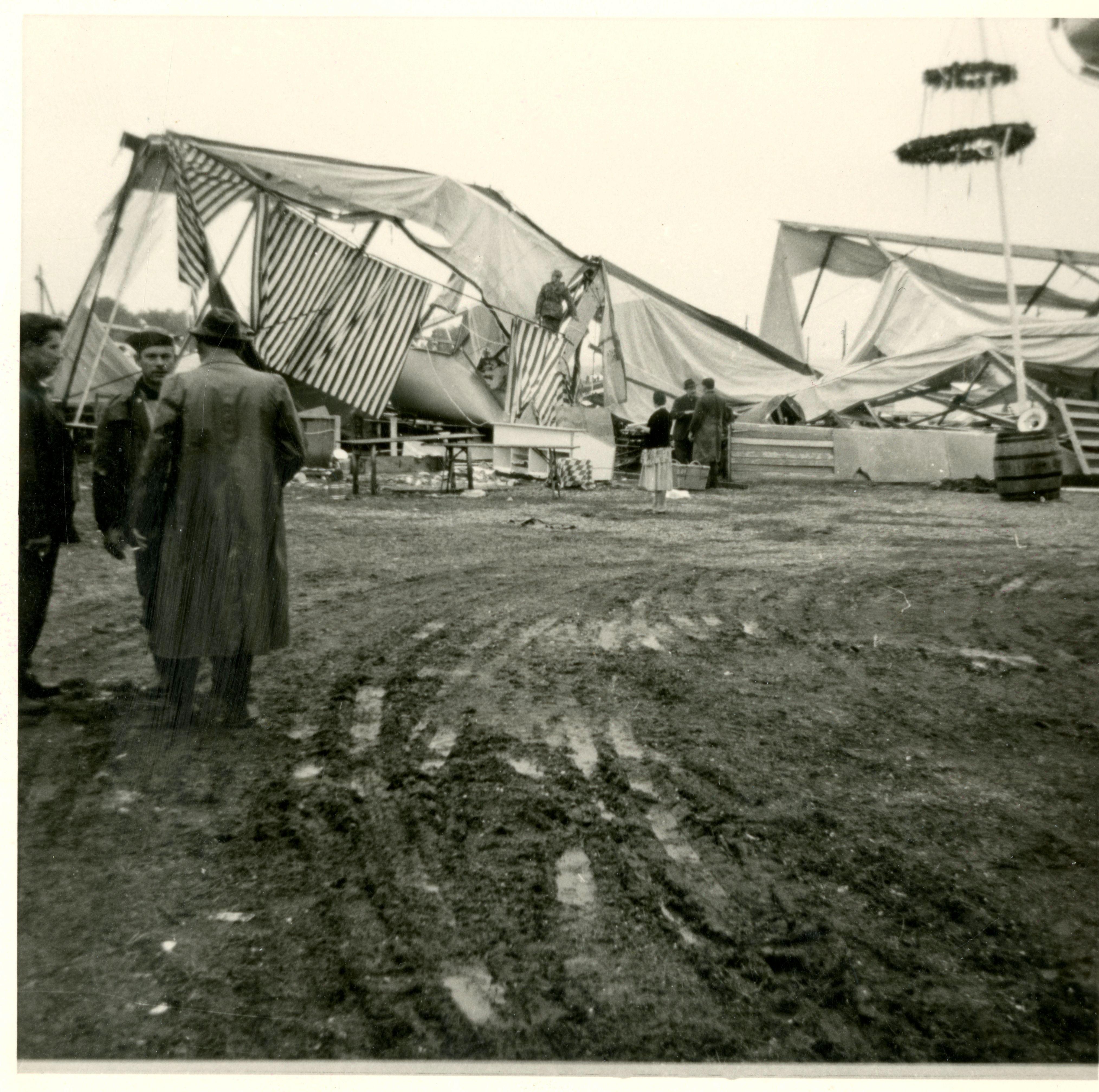 Das Bild ist alt. Im Vordergrund stehen drei Männer auf matschigem Boden. Hinten sieht man ein eingestürztes Festzelt.