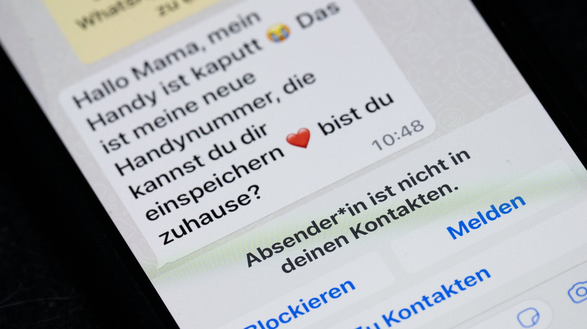 Symbolbild Trickbetrug: Auf dem Display eines Smartphones steht eine Whats App-Nachricht, die im Tonfall betrügerischen Nachrichten nachempfunden ist, die dazu genutzt werden, Geld zu bekommen.