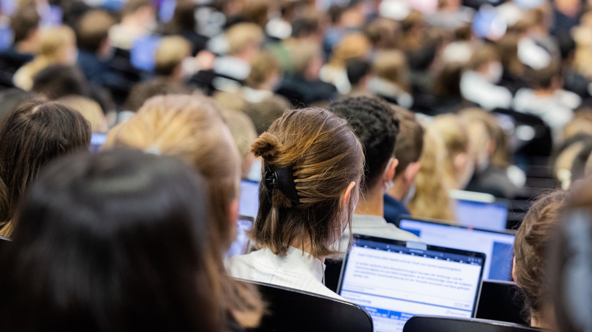 Studierende sitzen in einem Hörsaal. Vor ihnen stehen Laptopts. 