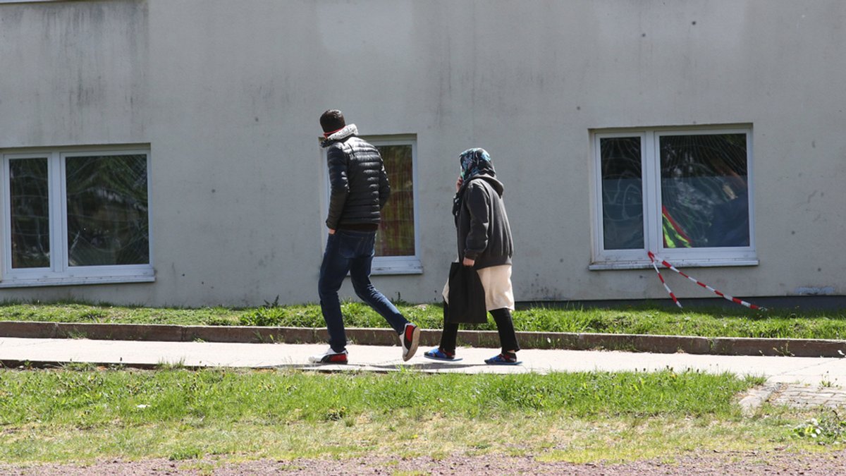 Ein Asylbewerber und eine Asylbewerberin gehen vor einer Erstaufnahmeeinrichtung spazieren
