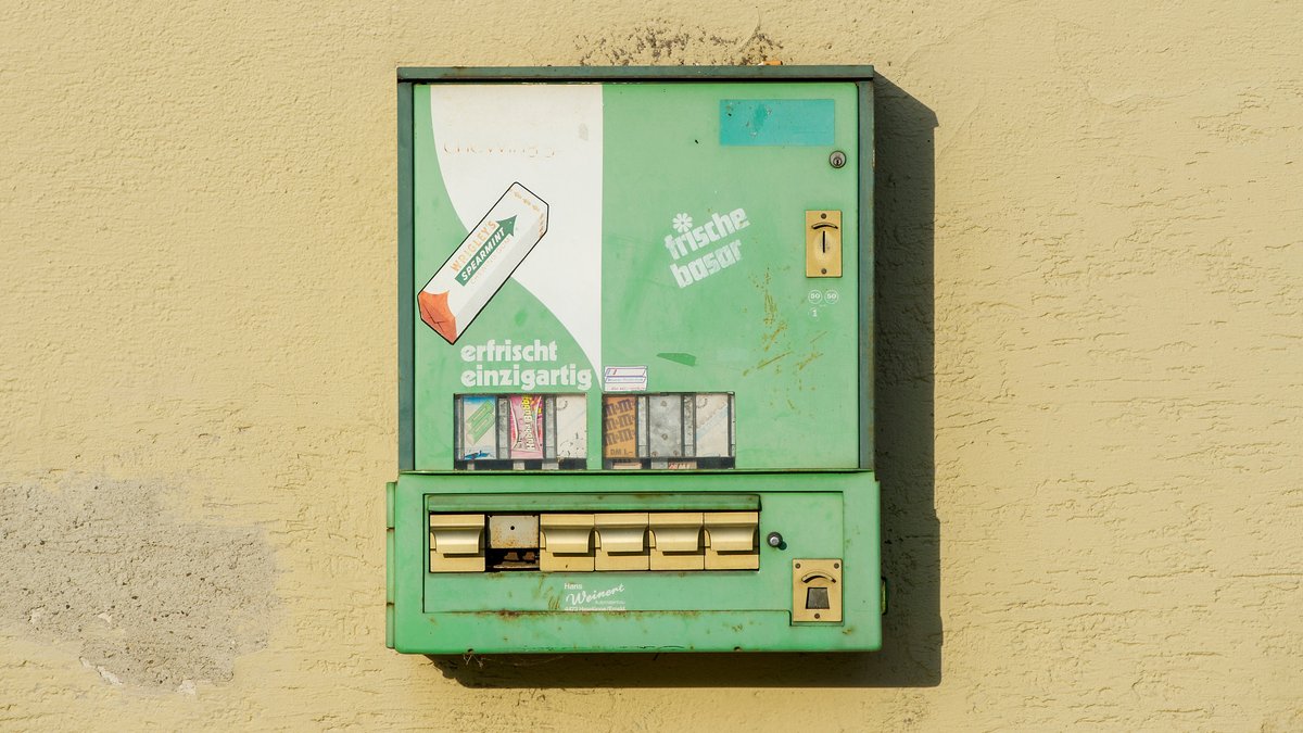 Ein alter Kaugummiautomat hängt an einer Wand. 
