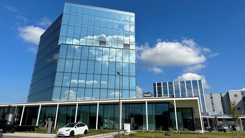 Vor einem 40 Meter hohen und vollverglasten Bürogebäude parkt ein Auto. 