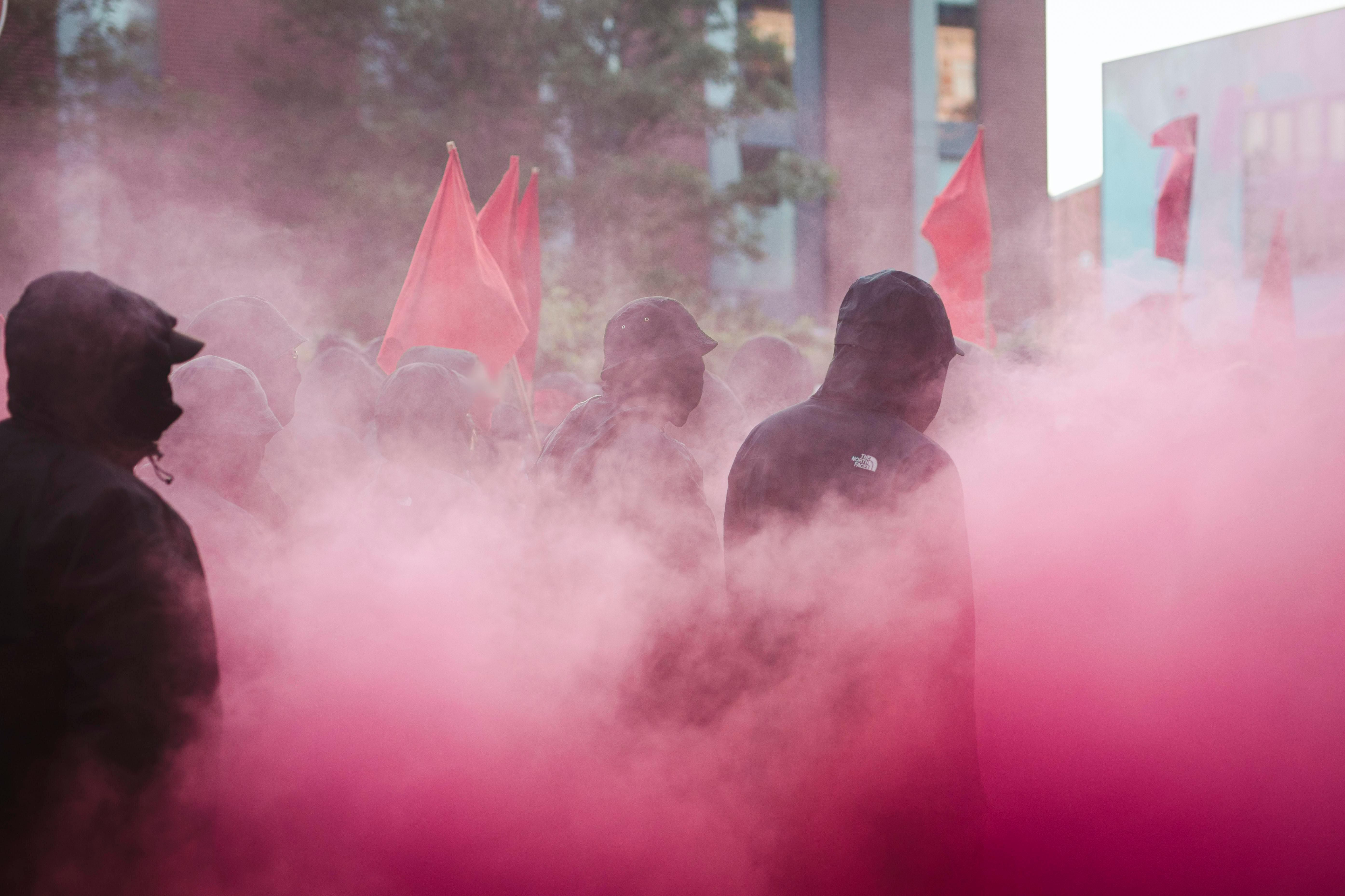 (Symbolbild) Vermummte Menschen in farbigem, roten Nebel 