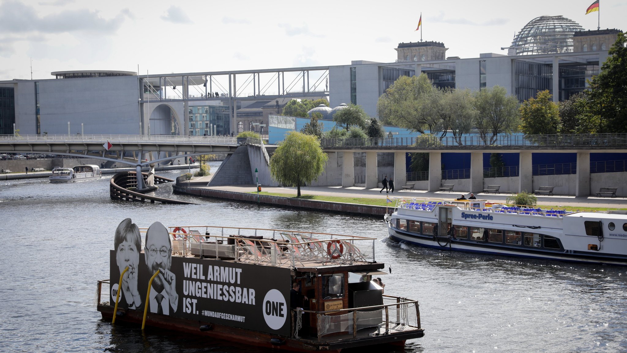 Ein Floß mit einem Großplakat mit den Konterfeis von Bundeskanzlerin Angela Merkel (CDU) und dem SPD-Kanzlerkandidat und Parteivorsitzende, Martin Schulz, fährt am 18.09.2017 in Berlin auf der Spree am Bundestag vorbei. Die Kampagnenorganisation One protestiert mit der Aktion "weil Armut ungenießbar ist" gegen Armut.