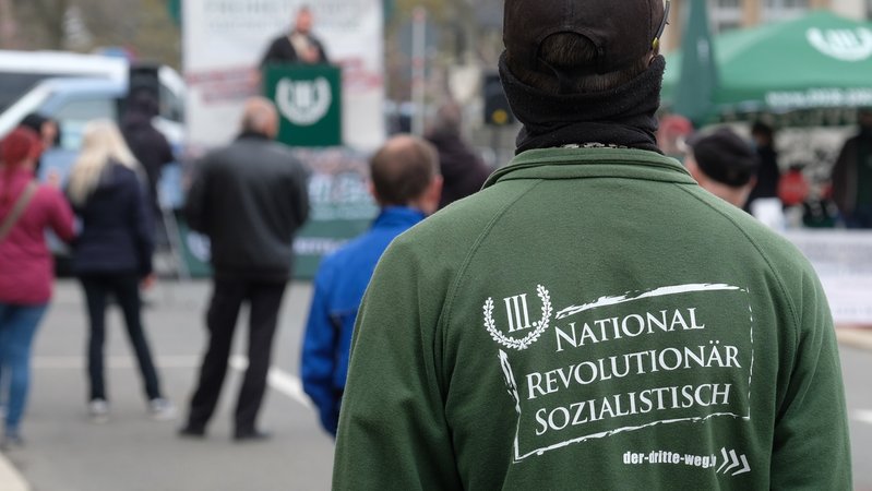 Ein Teilnehmer einer Kundgebung der rechtsextremen Partei "Der III. Weg" trägt eine Jacke mit der Aufschrift "National revolutionär sozialistisch".