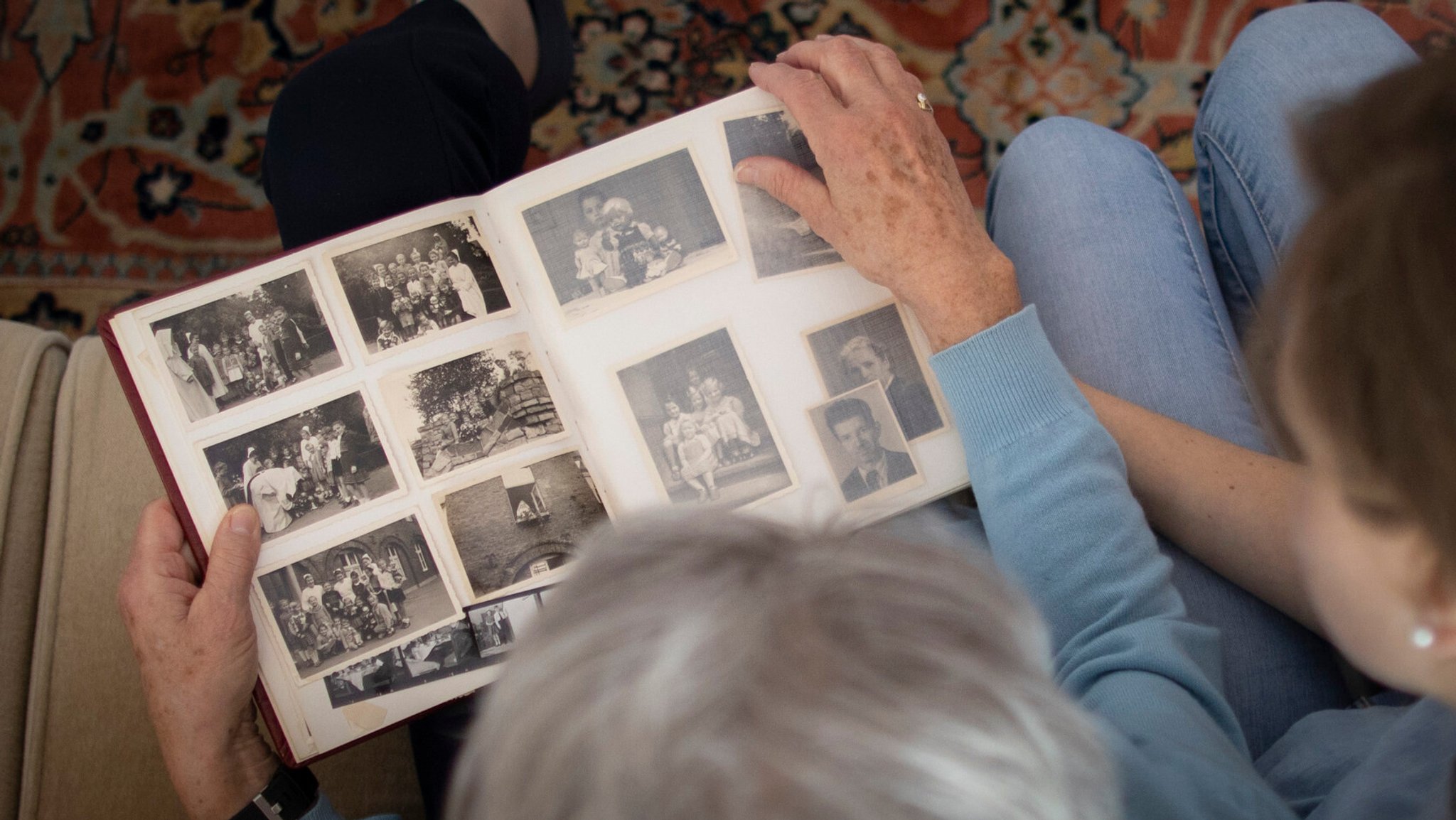 Eine ältere Frau und ein junger Mensch blicken in ein Fotoalbum voller Schwarz-Weiß-Fotos