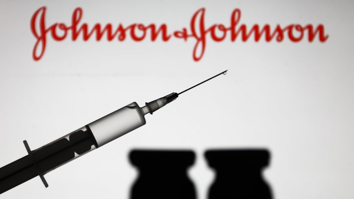 Einwegspritze mit Impfstoff und Johnson & Johnson-Schriftzug im Hintergrund