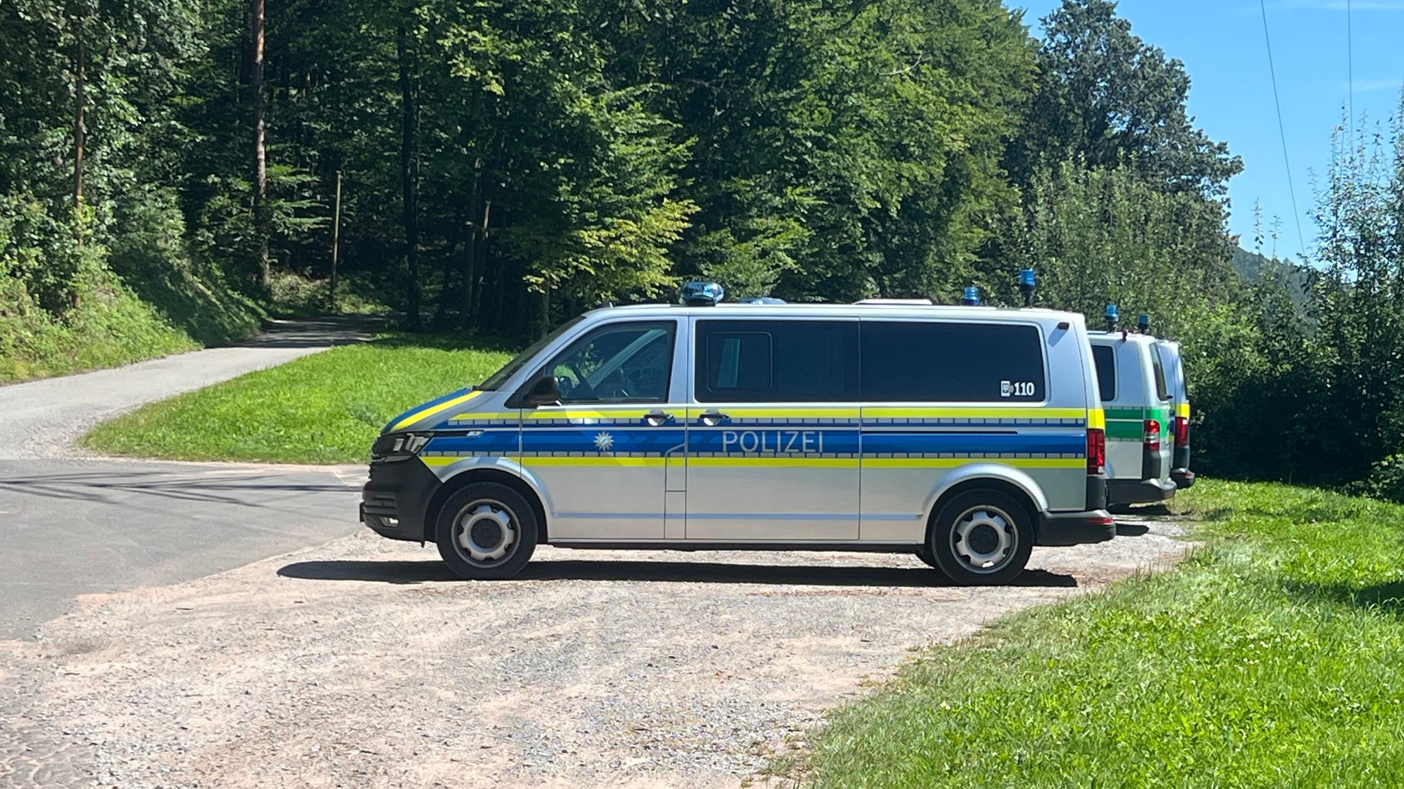 Polizeifahrzeuge auf einem Schotterparkplatz nahe eines Waldes