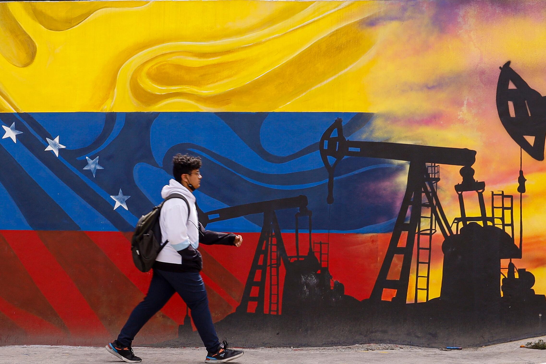 Ein Passant geht ein einem Wandgemälde vorbei, die Tiefpumpen zur Ölförderung über einer Flagge von Venezuela darstellt