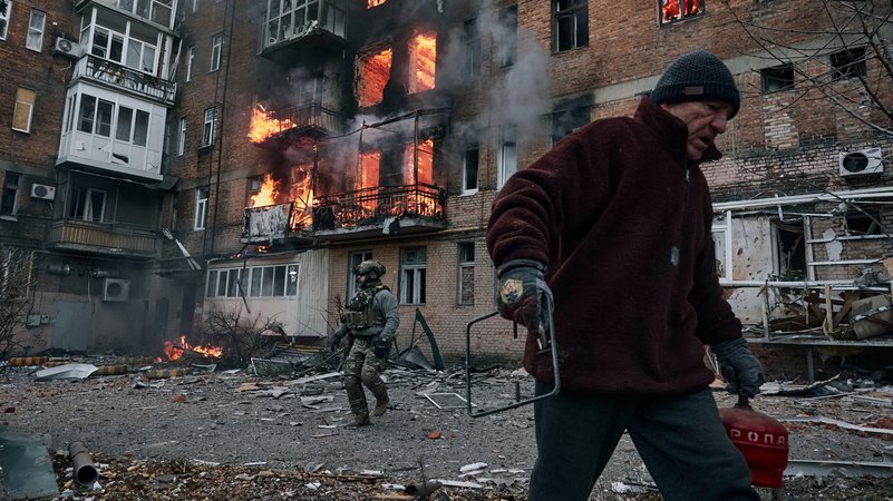 07.12.22: Ein Bewohner verlässt ein zerbombtes Haus in der Stadt Bachmut im Osten der Ukraine – vor dem brennenden Gebäude steht auch ein Soldat.