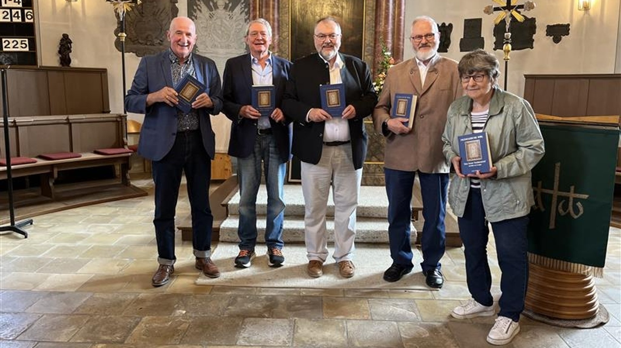 Ein Pfarrer steht mit vier anderen Menschen in der Kirche vor dem Altar. Sie halten je ein Exemplar der Fränksichen Bibel in den Händen.