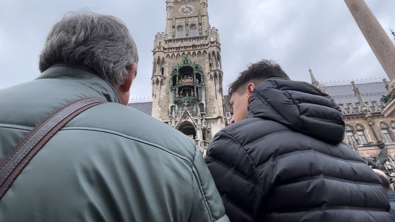 Zwei Touristen lauschen dem Glockenspiel am Neuen Rathaus am Marienplatz | Bild: BR / David Herting Zwei Touristen lauschen dem Glockenspiel am Neuen Rathaus am Marienplatz