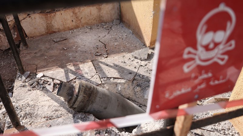 Der Rest einer Streubombe ist nach einem Angriff zu sehen, daneben ein Warn-Schild mit einem Totenkopf.