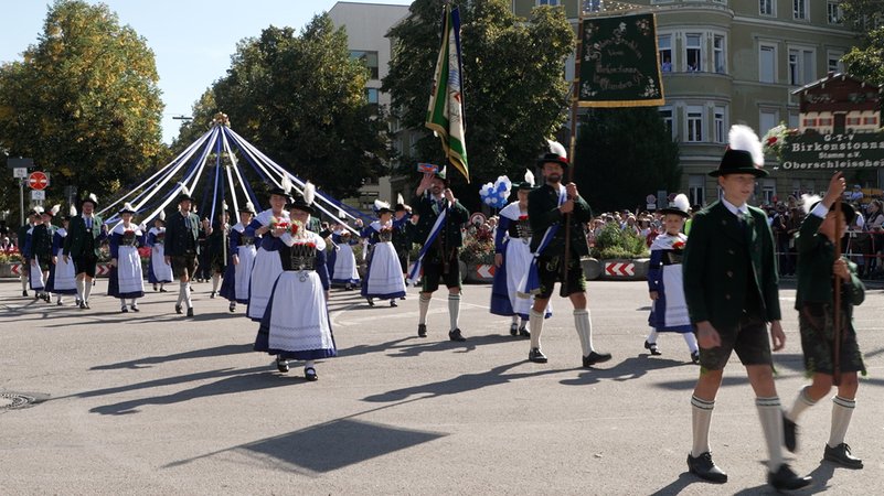 Eine Trachtengruppe im Trachten- und Schützenzug mit Standarten und geschmückten Bändern. 9.000 Menschen nahmen am Trachten- und Schützenzug zum Oktoberfest teil. | Bild: BR/Melina Eisemann Eine Trachtengruppe im Trachten- und Schützenzug mit Standarten und geschmückten Bändern. 9.000 Menschen nahmen am Trachten- und Schützenzug zum Oktoberfest teil.